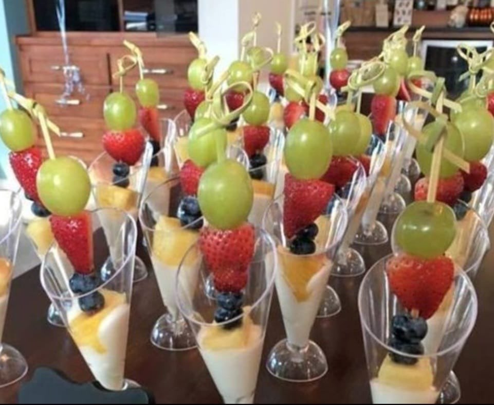 Rows of individual glasses topped with grape, strawberry and blueberry fruit skewers