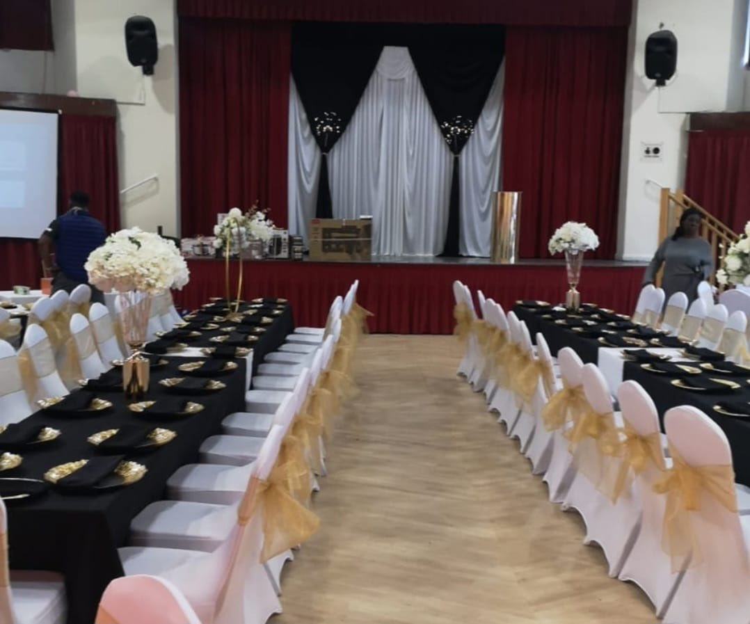 Event hall with black tablecloths, gold place settings, white chairs with gold bows and floral centrepieces